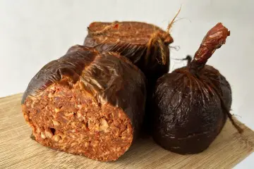 Trzy kawałki kalabryjskiej kiełbasy nduja, zawinięte w brązowy papier, na desce.