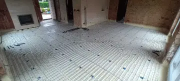 Installation d'un plancher chauffant en cours de renovation. Les tuyaux blancs sont posés sur des panneaux isolants, prêts à être recouverts.