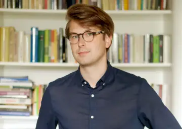 Mężczyzna w okularach na tle regałów z książkami. Czy to scholastyka?
