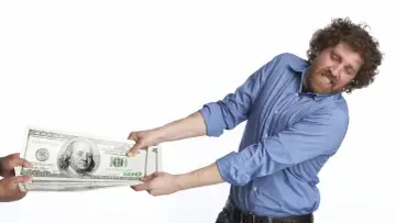 Mężczyzna z zakręconymi włosami i brodą szarpie stos banknotów dolarowych, jakby walczył o to, kto płaci czynsz za mieszkanie.