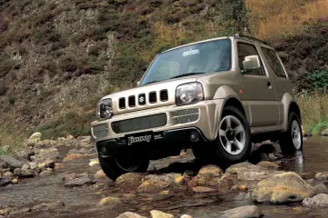 Złoty Suzuki Jimny pokonuje kamienisty strumień. Sprawdź suzuki jimny cena i możliwości terenowe tego kultowego auta.