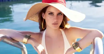 Lana Del Rey, wokalistka, w letnim kapeluszu i biżuterii, relaksuje się przy basenie.