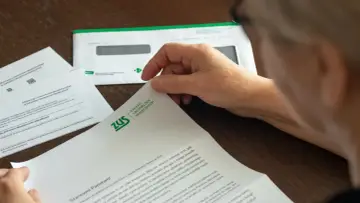 Osoba czyta dokument ZUS, który może być decyzją o przyznaniu emerytury. Widać logo ZUS i fragmenty tekstu.