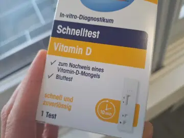 Hand hält eine Verpackung für einen Vitamin-D-Schnelltest mit einem Bluttest-Streifen.