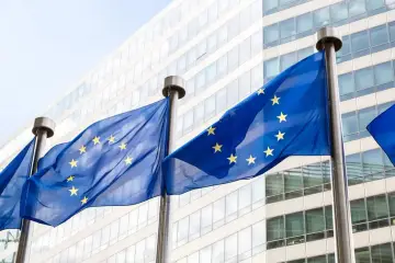 Flagi Unii Europejskiej powiewają przed nowoczesnym budynkiem, symbolizując jedność i współpracę krajów unii europejskiej.