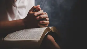 Dłonie złożone do modlitwy nad otwartą Biblią. Odmawiany jest cały pacierz po kolei, szukając pocieszenia i siły w słowach Pisma Świętego.