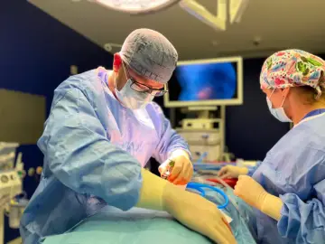 Chirurg wykonuje operację przepukliny, skupiony na precyzyjnym działaniu. W tle monitor pokazuje obraz z wnętrza ciała.