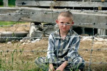 Pojken i randig pyjamas, Shmuel, sitter bakom taggtråd. Hans ansikte är smutsigt och hans blick är sorgsen.
