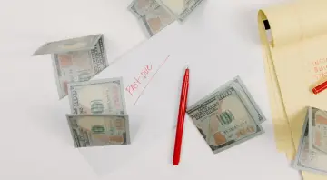 Na stole leżą banknoty 100 USD, czerwony długopis i notatnik. Na kartce papieru widnieje napis "Past Due". To może być faktura imienna z zaległą płatnością.