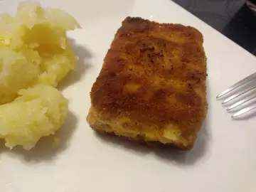 Chrupiąca panierowana kostka rybna z purée ziemniaczanym na białym talerzu.