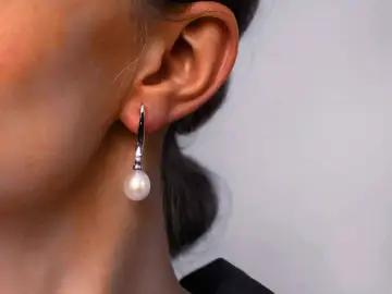 Eleganckie kolczyki z perłą, wiszące przy uchu. Delikatny piercing podkreśla piękno biżuterii.