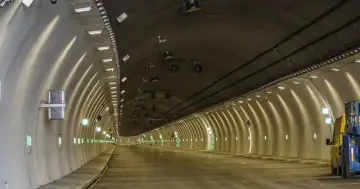 Nowy tunel na Zakopiance, oświetlony rzędem zielonych świateł i lamp, z widocznym żółtym pojazdem budowlanym.