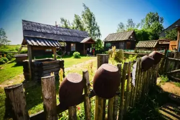 Skansen na wyżynie krakowsko-częstochowskiej: drewniane chaty, studnia i gliniane garnki na płocie.