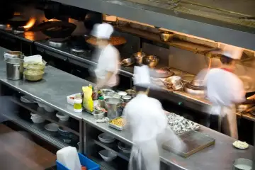 Chefs en movimiento en una cocina profesional, con ollas humeantes y ingredientes listos. El "mise en place" es clave para la eficiencia.