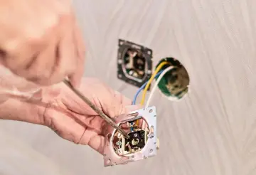 Ręce majsterkowicza montują mechanizm włącznika, przygotowując instalację, jak podłączyć światło na dwa włączniki.