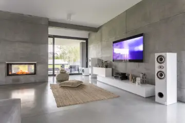 Nowoczesny salon z betonowymi ścianami, kominkiem i dużym telewizorem 70 cali. Wymiary tego ekranu robią wrażenie!