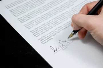 Dłoń podpisuje dokument piórem. Czy czynsz płaci się co miesiąc? To pytanie może pojawić się przy podpisywaniu umowy.