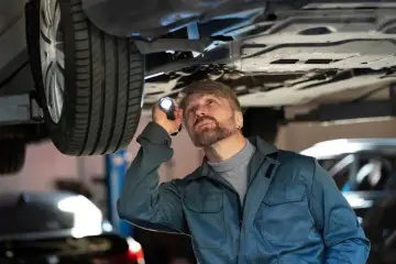 Mechanik z latarką bada podwozie auta, szukając problemów z jarzmem hamulca.