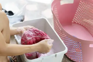 Ręczne pranie zafarbowanego na czerwono ubrania w wodzie z mydłem. Domowy sposób, jak odratować zafarbowane w praniu białe ubranie.