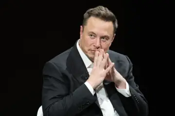Elon Musk, uważany za najbogatszego człowieka na świecie, w garniturze, z dłońmi złożonymi przed twarzą.