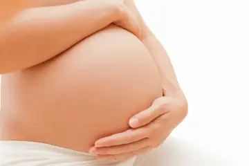 Dłońmi obejmuje zaokrąglony brzuch, w którym dziecko ułożyło się w położenie podłużne główkowe.