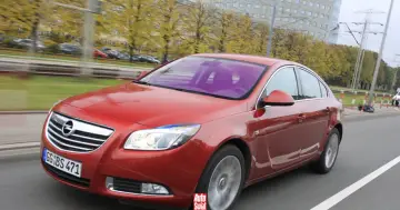 Czerwony Opel Insignia 1.6 Turbo w ruchu ulicznym. Wady tego modelu mogą dotyczyć np. spalania.