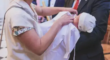 Dziecko w bieli otulone przez rodziców, symboliczne skutki przyjęcia chrztu.