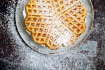 Herzförmige Waffeln, bestäubt mit Puderzucker, auf einem Teller. Ein köstliches Rezept für süße Momente.