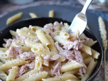 Penne z kremowym sosem i kawałkami szynki parmeńskiej, posypane parmezanem i pieprzem. Widok z bliska na apetyczne danie.