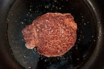 Ein saftiges Steak brutzelt in der Pfanne, bestreut mit grobem Salz.