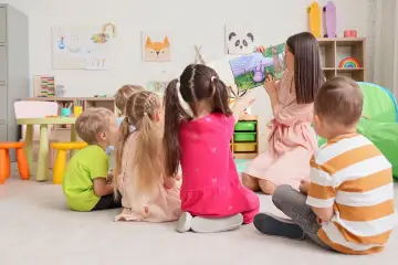 Nauczycielka czyta dzieciom bajkę. W przedszkolu bezpłatnych godzin jest 5.
