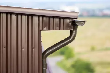 Nowy, brązowy system rynnowy zamontowany na ścianie starego domu. Wymiana rynien poprawia estetykę i funkcjonalność.