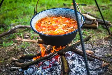 Aromatyczny gulasz z kociołka gotuje się nad ogniskiem, wśród zieleni.