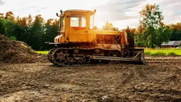 Żółty spychacz na placu budowy. Zastanawiasz się, ile kosztuje wyrównanie terenu pod budowę? Maszyna gotowa do pracy.