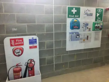 Tablica informacyjna budowy z gaśnicami, apteczką i instrukcjami.