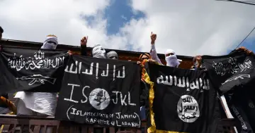 Osoby z zasłoniętymi twarzami trzymają czarne flagi z napisami w języku arabskim i angielskim, w tym "Islamic State of Jammu Kashmir & Ladakh".