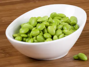 Miseczka pełna zielonej fasolki edamame na drewnianym tle.
