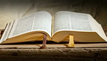 Otwarta księga, być może Stary Testament, z zaznaczonymi fragmentami. Widać tekst, grube, pożółkłe strony i dwie wstążki.