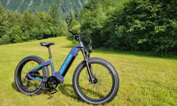 Fioletowy rower elektryczny RATTAN Sequoia na tle zielonych wzgórz. Idealny do odkrywania nowych szlaków, zgodnie z przepisami ruchu drogowego.