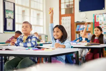 Dzieci na lekcji, jedna dziewczynka podnosi rękę, zastanawiając się, kiedy złożyć wniosek o wydłużenie etapu edukacyjnego.