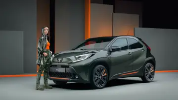 Stylowa kobieta obok zielonego Aygo X. Czy to auto spełnia **toyota aygo opinie**? Nowoczesny design i miejski charakter.