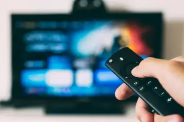 Ręka trzymająca pilot do telewizora, gotowa do nauki, jak zainstalować aplikacje na telewizorze.