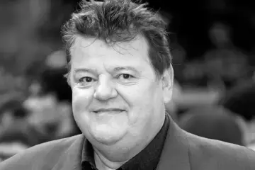 Uśmiechnięty Robbie Coltrane, aktor znany z roli Hagrida, w czarno-białym portrecie.