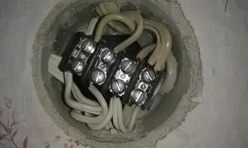Widok z góry na puszkę instalacyjną z połączonymi kablami. Widać kostkę elektryczną z sześcioma śrubami, do której podłączone są białe przewody.