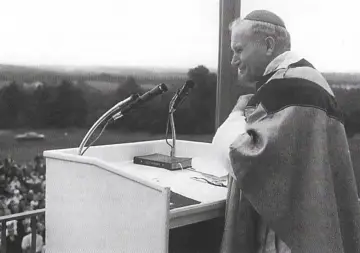Jan Paweł II przy mównicy, gotów do recytacji wierszy Karola Wojtyły. Tłum słuchaczy w tle.