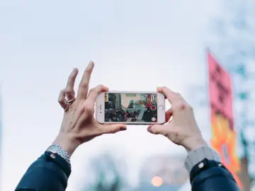 Dłonie trzymają iPhone'a w poziomie, nagrywając tłum. Dowiedz się, jak obrócić ekran w iPhone, by uchwycić szerszy kadr.