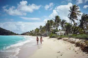 Dwie kobiety spacerują po piaszczystej plaży z palmami. Idealny czas na Karaiby kiedy jechać to okres od grudnia do maja.