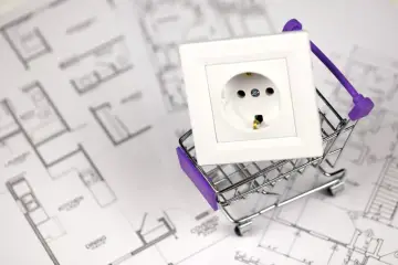 Biały włącznik światła pojedynczy w miniaturowym wózku sklepowym na tle planów architektonicznych.