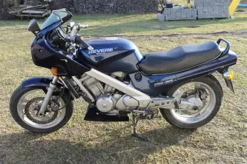 Granatowy motocykl Honda NTV Revere z napędem wałowym, zaparkowany na trawie.