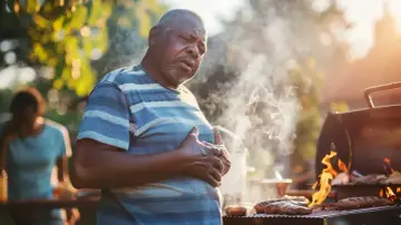Mężczyzna z bólem w klatce piersiowej przy grillu. Może szuka czegoś, co neutralizuje kwas żołądkowy po obfitym posiłku.